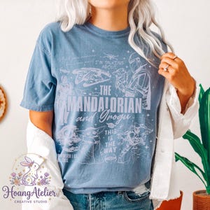 Puede incluir: Una camiseta azul claro con un dise&ntilde;o gr&aacute;fico con el texto "The Mandalorian and Grogu". El dise&ntilde;o incluye ilustraciones de personajes y elementos de la serie Star Wars. La camiseta tambi&eacute;n tiene las frases "I'm talking about" y "This is the way."