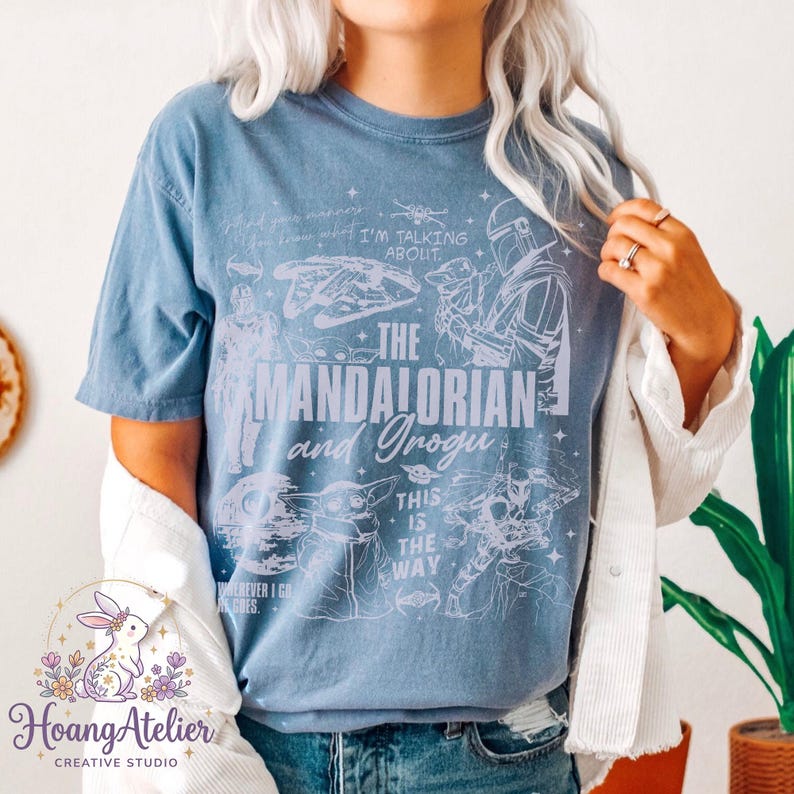 Puede incluir: Una camiseta azul claro con un dise&ntilde;o gr&aacute;fico con el texto "The Mandalorian and Grogu". El dise&ntilde;o incluye ilustraciones de personajes y elementos de la serie Star Wars. La camiseta tambi&eacute;n tiene las frases "I'm talking about" y "This is the way."