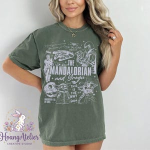 Puede incluir: Camiseta verde oliva con el texto "THE MANDALORIAN and Grogu" e ilustraciones de personajes de la serie. La camiseta tambi&eacute;n incluye las frases "This is the Way" y "Wherever I Go, He Goes."