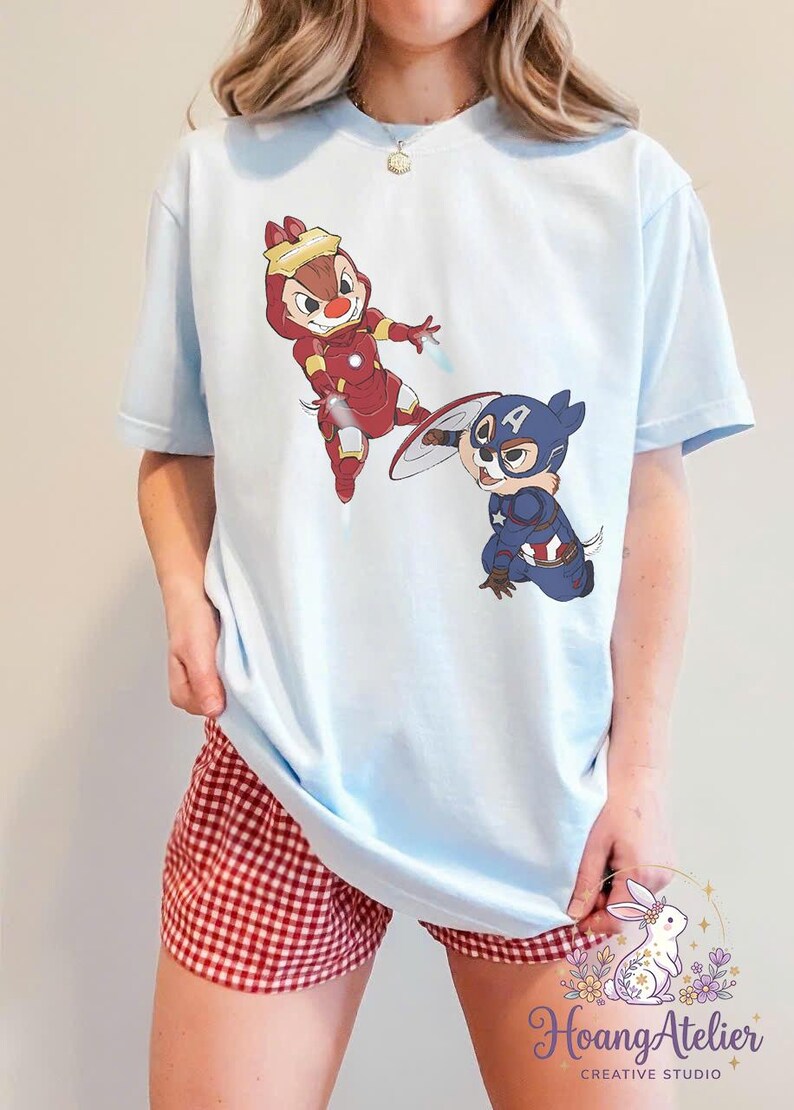 May include: Light blue t-shirt featuring cartoon characters dressed as superheroes. One character is in a red Iron Man suit, and the other is in a Captain America costume. The shirt is paired with red and white checkered shorts.