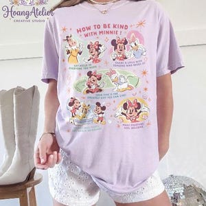 May include: A lilac t-shirt with a graphic of Minnie Mouse and friends, and the text "HOW TO BE KIND WITH MINNIE!". The design includes illustrations and phrases such as "Say hello to everyone you meet!" and "Share a smile with someone who needs it!"