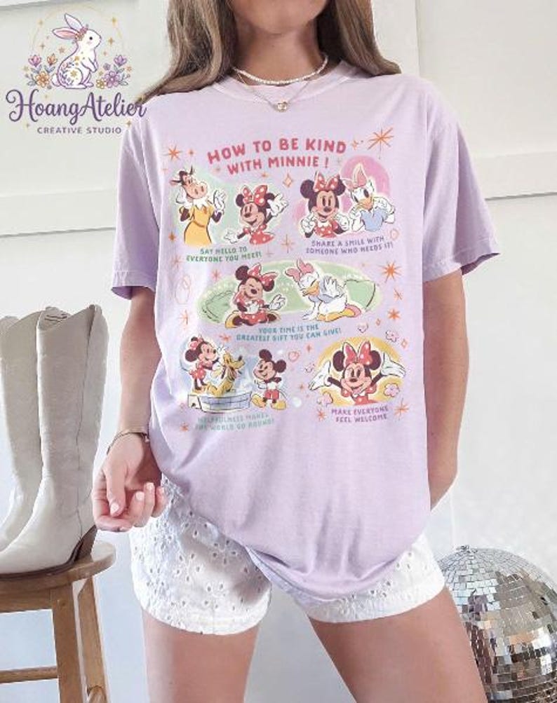 May include: A lilac t-shirt with a graphic of Minnie Mouse and friends, and the text "HOW TO BE KIND WITH MINNIE!". The design includes illustrations and phrases such as "Say hello to everyone you meet!" and "Share a smile with someone who needs it!"