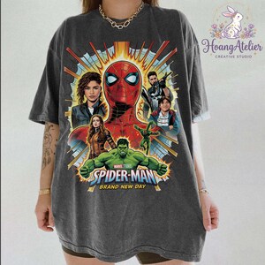 May include: Dark gray t-shirt featuring a graphic of Spider-Man and other Marvel characters. The design includes the text "Spider-Man Brand New Day". The shirt has a vintage, distressed look.