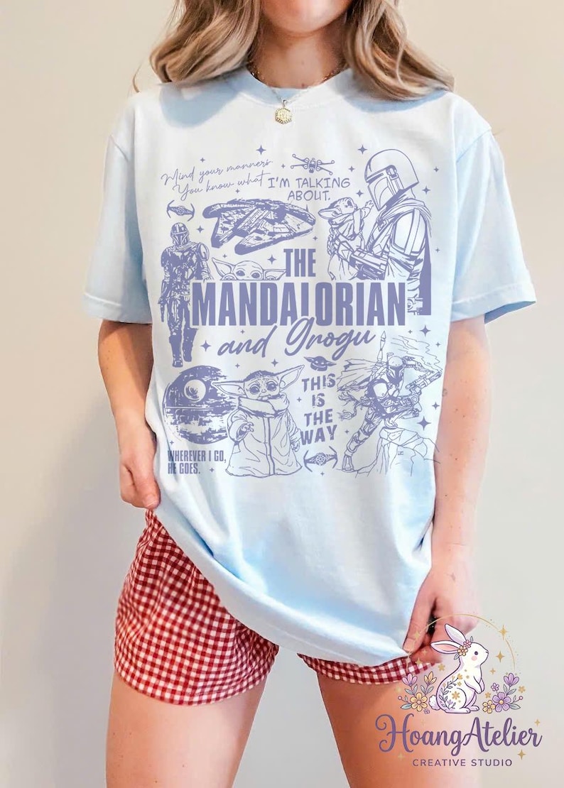 Puede incluir: Camiseta azul claro con ilustraciones de "The Mandalorian", incluyendo al Mandaloriano y Grogu, y el texto "The Mandalorian and Grogu". La camiseta tambi&eacute;n tiene las frases "Mind your manners" y "This is the way".