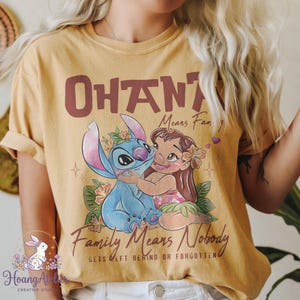 Op de afbeelding: Mosterdgeel T-shirt met een afbeelding van Stitch en Lilo uit de Disney-film Lilo & Stitch. De tekst "OHANA Means Family" en "Family Means Nobody Gets Left Behind or Forgotten" staat boven en onder de afbeelding.
