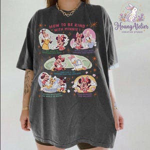 May include: Dark grey t-shirt with Minnie Mouse and friends, and the text "HOW TO BE KIND WITH MINNIE!". The shirt features illustrations of Minnie, Daisy, and other characters with positive messages. The Hoang Atelier logo is in the upper right corner.