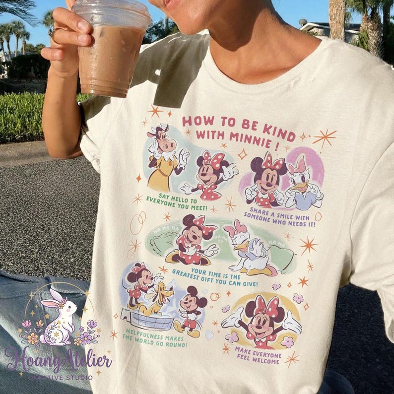 May include: Cream-coloured t-shirt with a graphic featuring Minnie Mouse and friends. The graphic includes the text "HOW TO BE KIND WITH MINNIE!" and kindness tips. A casual, everyday wear item.