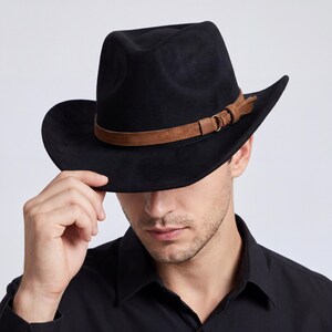 May include: A black cowboy hat with a brown leather band and buckle. The hat has a wide brim and a classic western design. The hat is made of a soft material.