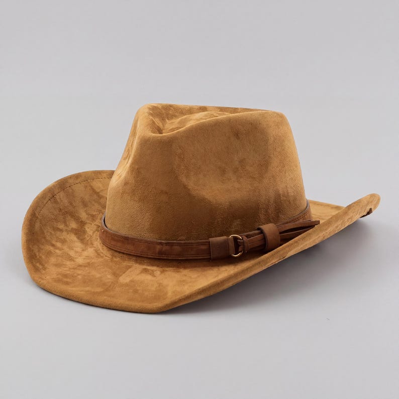May include: A tan suede cowboy hat with a brown leather band and buckle. The hat has a wide brim and a slightly indented crown. The hat is a classic western style.