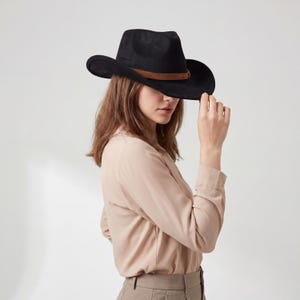 May include: A black cowboy hat with a brown band. The hat has a wide brim and a classic shape. The hat is made of a soft material and is a stylish accessory.