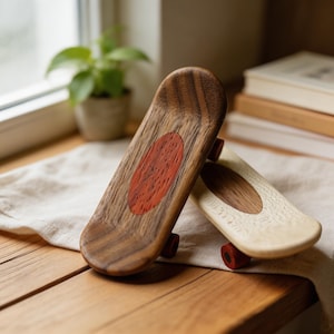 Peut inclure: Deux mini-skateboards en bois. L'un est brun foncé avec un incrustation ovale rouge et des roues rouges. L'autre est brun clair avec une incrustation ovale plus claire et des roues rouges. Ils reposent sur une surface en bois.