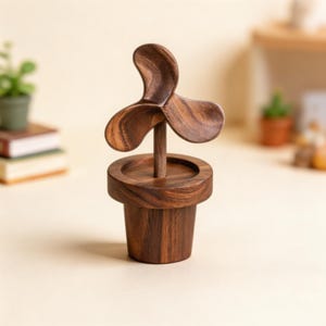 May include: A wooden sculpture of a plant in a pot. The sculpture has a three-blade fan design on a wooden stem, set in a cylindrical pot. The wood is a dark brown colour, and the piece is set against a neutral background. The pot is approximately 7 cm tall.