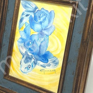 以下が含まれることがあります： 青い金魚と青い花が黄色い背景に描かれた額入りの水彩画。 このアートワークは、濃い青と茶色の木製フレームに収められており、家の装飾用の装飾品を作成しています。