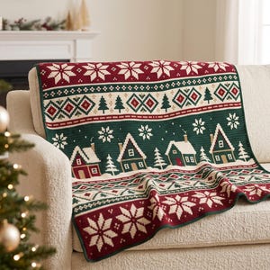 May include: A rectangular knit throw blanket featuring a festive holiday pattern with dark green, deep red, and cream colours. The design includes rows of white snowflakes, geometric diamond shapes, evergreen trees, and a village of small houses.