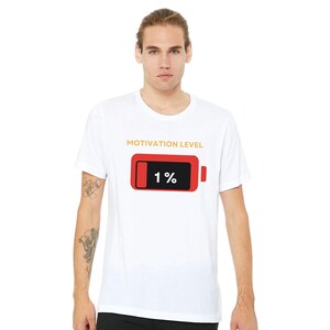Könnte beinhalten: Weißes T-Shirt mit dem Text "MOTIVATION LEVEL" über einer roten Batterie-Grafik, die 1 % Ladung anzeigt. Das Shirt hat einen Rundhalsausschnitt und wird von einer Person getragen.