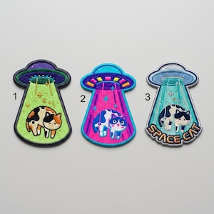 May include: Three embroidered patches featuring cats being abducted by UFOs. Patch 1 is green with a calico cat. Patch 2 is pink with a blue and white cat. Patch 3 is light blue with a black and white cat and the text SPACE CAT at the bottom.