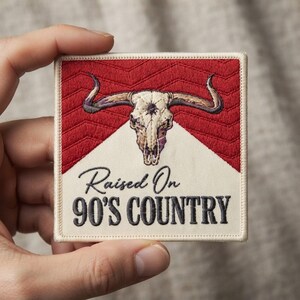 May include: A square embroidered patch featuring a cream-colored background with a red chevron-patterned top section. Centered is a detailed steer skull with long horns. Below the skull, the text reads Raised On 90'S COUNTRY in black.