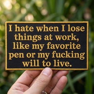 May include: A rectangular black embroidered patch with a gold border and gold text that reads: I hate when I lose things at work, like my favorite pen or my fucking will to live. The patch features a clean, bold font and a durable stitched edge.