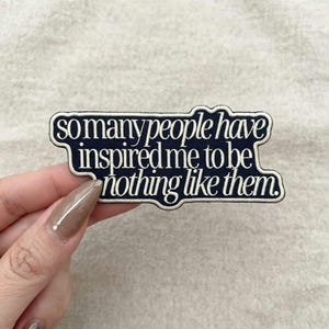 May include: A dark navy blue embroidered patch with a cream-colored border and the white text "so many people have inspired me to be nothing like them." The patch has a custom die-cut shape that follows the contour of the lettering.