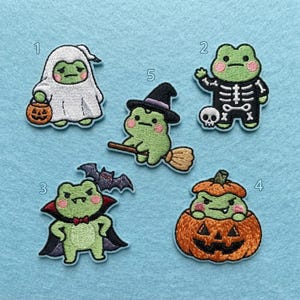 May include: Five embroidered patches featuring green frogs in Halloween costumes. Patch 1 is a ghost with a pumpkin bucket, 2 is a skeleton, 3 is a vampire with a bat, 4 is a frog in a jack-o'-lantern, and 5 is a frog on a broomstick.