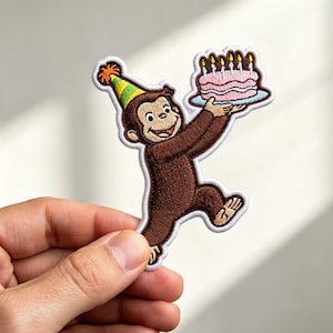 May include: An embroidered patch featuring a brown monkey wearing a green and yellow striped party hat with an orange pom-pom. The monkey is smiling and holding a pink frosted birthday cake with six lit candles on a light blue plate.