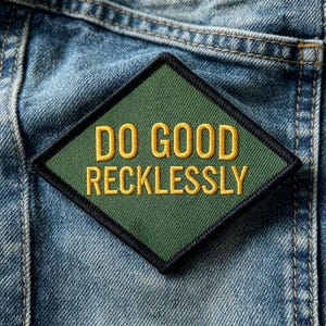 May include: A diamond-shaped embroidered patch with a dark green background and a black border. The text DO GOOD RECKLESSLY is stitched in bold yellow capital letters across the center of the patch, which is placed on blue denim fabric.