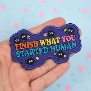 May include: A dark blue embroidered patch with a wavy edge featuring the text FINISH WHAT YOU STARTED HUMAN in orange, yellow, and light blue. The design includes four small black fuzzy creatures holding yellow stars and a pink cupcake.
