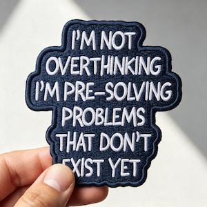May include: A dark navy blue embroidered patch with a scalloped edge featuring the white stitched text: I'M NOT OVERTHINKING I'M PRE-SOLVING PROBLEMS THAT DON'T EXIST YET. The patch has a thick, raised border and a dense, textured fabric construction.