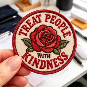 May include: A circular embroidered patch with a cream-colored background and a red border. The center features a detailed red rose with green leaves. The text "TREAT PEOPLE WITH KINDNESS" is stitched in red around the rose.