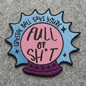 May include: Embroidered patch featuring a pink crystal ball with the text "FULL OF SH*T" in black. The crystal ball is surrounded by a blue burst design with the text "CRYSTAL BALL SAYS YOU'RE". The patch has a purple base.