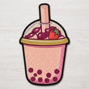 May include: An embroidered patch shaped like a bubble tea cup with a light pink drink, dark purple tapioca pearls at the bottom, a gold rim, and a top layer of dark purple cream topped with a single red strawberry and a light pink straw.