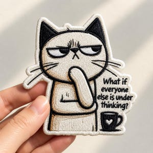 May include: An embroidered patch featuring a tan cat with black ears and a grumpy expression. The cat has one paw to its chin in a thinking pose. Next to the cat is a black coffee mug with a white heart and the text: What if everyone else is under thinking?