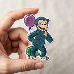 May include: An embroidered patch featuring a dark teal monkey with a light tan face, hands, and feet. The monkey is smiling, holding a purple balloon in one hand, and standing in front of a green balloon. The patch has a white border.