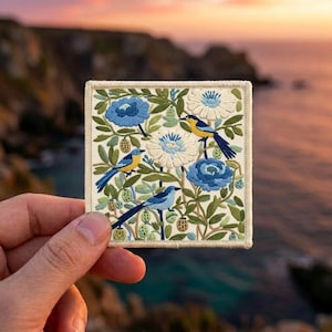 May include: A square embroidered patch featuring three small birds perched among blue and white flowers and green foliage. The design is stitched with detailed thread work on a cream-colored fabric base with a finished stitched border edge.