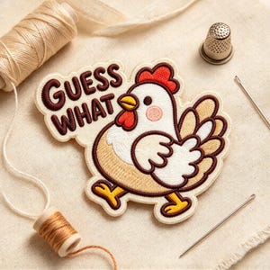 May include: An embroidered patch featuring a white and tan chicken with a red comb and wattle, and the text GUESS WHAT in dark brown. The patch is surrounded by a spool of tan thread, a silver thimble, and a long sewing needle.