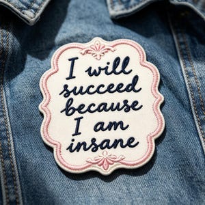 May include: A cream-colored embroidered patch with a scalloped pink border and decorative flourishes. The patch features the dark blue text "I will succeed because I am insane" in a cursive script, centered on a blue denim fabric background.