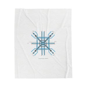 Op de afbeelding: Witte deken met een blauw en zwart geometrisch ontwerp. Het ontwerp toont een netwerk van lijnen en vormen, dat lijkt op een stadsplattegrond of een printplaat. De deken heeft een zacht, getextureerd uiterlijk.