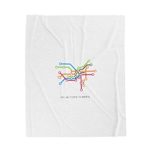 May include: White blanket featuring a colorful graphic of the NYC subway system map. The map includes lines in blue, green, orange, pink, and brown. The text "NYC 40.7128°N 74.0060°W" is printed below the map.