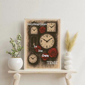 Op de afbeelding: Ingelijste kunstafdruk met meerdere klokken en rode rozen tegen een neutrale achtergrond. De witte tekst luidt "Everything Comes In Its Own TIME". Het kunstwerk wordt tentoongesteld op een lichtgekleurde houten plank.