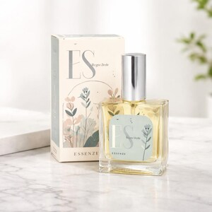 Pode incluir: Um frasco de perfume de vidro transparente com tampa prateada e caixa a condizer. O frasco e a caixa apresentam as letras "ES" e as palavras "Regno Verde" e "Essenze". A caixa tem um design floral.