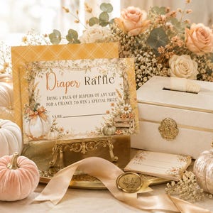 May include: A Diaper Raffle sign with floral and pumpkin illustrations, reading "Diaper Raffle. Bring a pack of diapers of any size for a chance to win a special prize." The sign is displayed on a gold stand next to a cream-colored box with a slot.