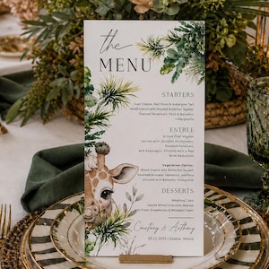 May include: A wedding menu card with a giraffe illustration and botanical accents. The menu lists starters, entrees, and desserts. The card is set on a table with gold cutlery, plates, and a decorative giraffe figurine.