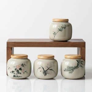 May include: Four ceramic jars with wooden lids, arranged on a wooden shelf. The jars are a light beige color and feature hand-painted floral and botanical designs in pink and green. The jars are of varying sizes.