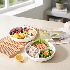 May include: Two white divided plates with various foods, including berries, salad, corn, prawns, rice, and vegetables. A glass of water with lemon and rosemary, a wooden serving board, and wooden cutlery are also present.