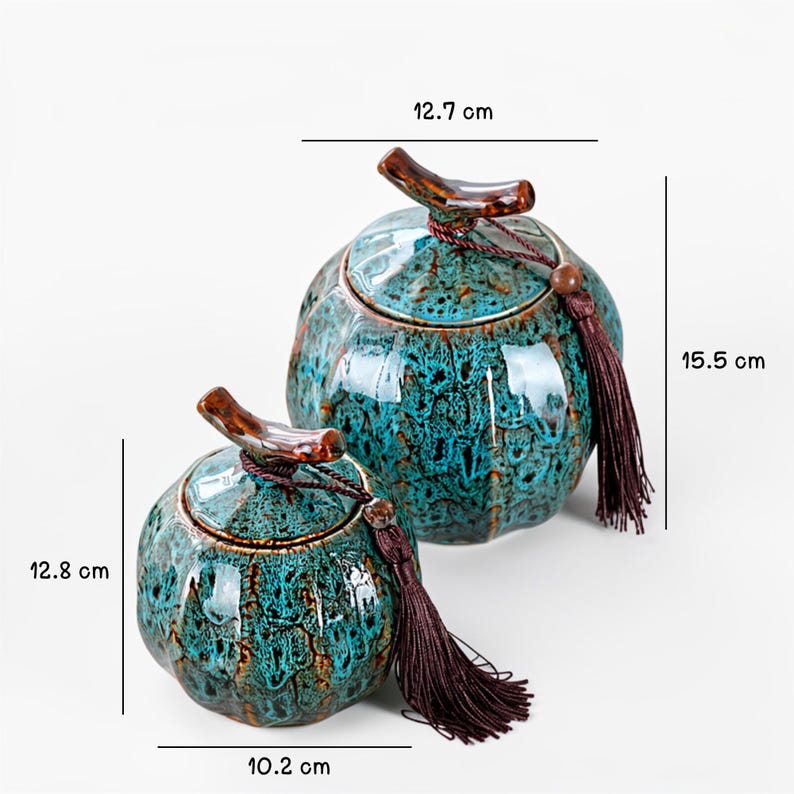 May include: Two ceramic jars with lids, featuring a teal and brown mottled glaze. The larger jar is 15.5 cm tall and 12.7 cm wide, while the smaller jar is 12.8 cm tall and 10.2 cm wide. Each jar has a brown wooden handle and a tassel.
