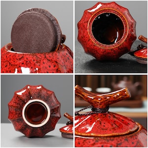 May include: A red ceramic tea caddy with a textured, speckled finish. The caddy has a unique, ridged shape and a matching lid with a wooden handle. A brown, circular tea bag is visible inside.