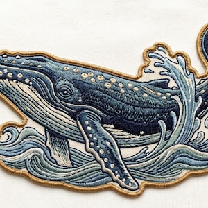 May include: Embroidered patch featuring a blue whale breaching the ocean waves. The whale is detailed with white accents and a tan border. The patch is designed with shades of blue and white, creating a nautical theme.