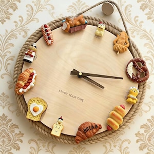Op de afbeelding: Een ronde houten klok met een touwrand, met voedselthema decoraties zoals een croissant, een pretzel en een hotdog. De wijzerplaat heeft de tekst "ENJOY YOUR TIME". De wijzers zijn bruin.