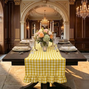 Könnte beinhalten: Ein Esstisch ist mit einem gelb-weiß karierten Tischläufer, Tellern, Besteck und Kristallgläsern gedeckt. Ein Blumenarrangement und brennende Kerzen schmücken den Tisch, mit einem Kronleuchter darüber.