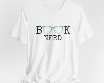 May include: White t-shirt with a black graphic that says "BOOK NERD" with a pair of green glasses.